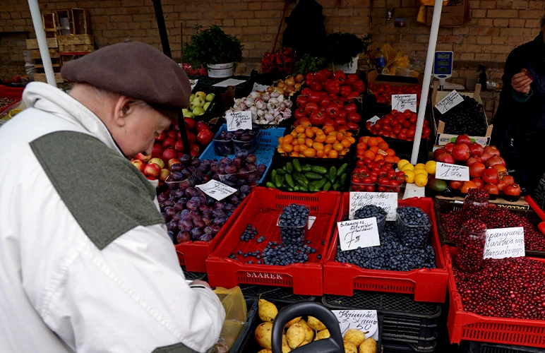 An older man in a beret counting change in his hand in front of a fruit and vegetable stall