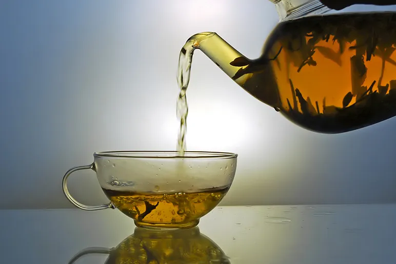 Tea being poured from a clear teapot into a clear tea cup