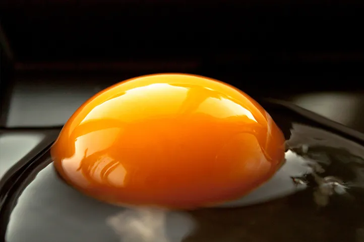 A closeup of a bright yellow egg yolk sitting in a dark pan