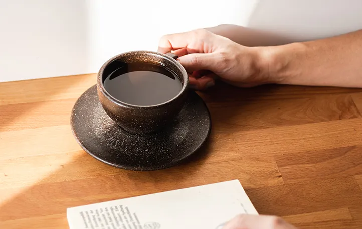 Man holding cup of coffee next to open book