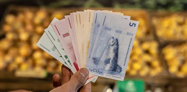 A hand fanning out a selection of currency in front of a display of potatoes