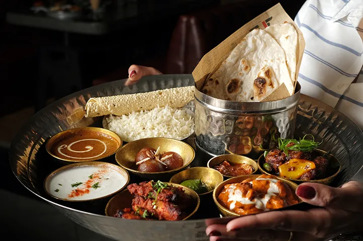 Metal tray of Indian food in various containers being carried by a woman