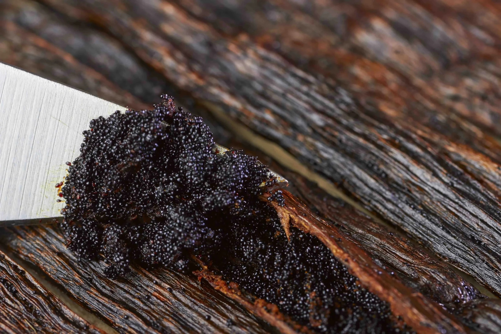 Vanilla beans being scooped by metal knife on wooden board